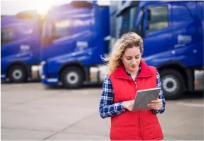 A transport worker with a tablet in front of a line of blue lorries